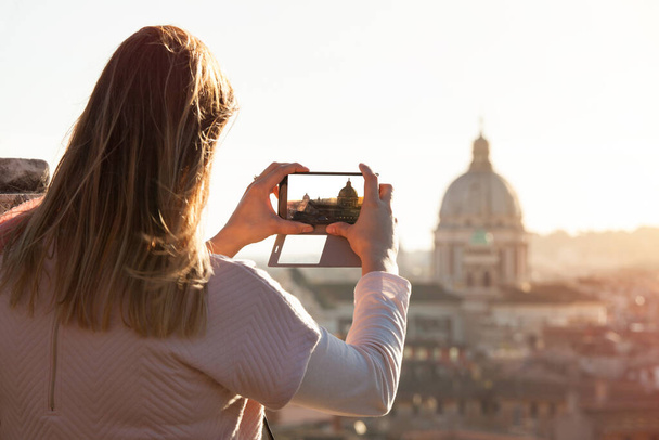 Turist kadın akıllı telefon çekiyor. Roma 'ya, İtalya' ya git. Roma şehrine fotoğraf çektiren bir turist kadın. Aziz Peter Kubbesi ve şehir manzarası yukarıdan. - Fotoğraf, Görsel