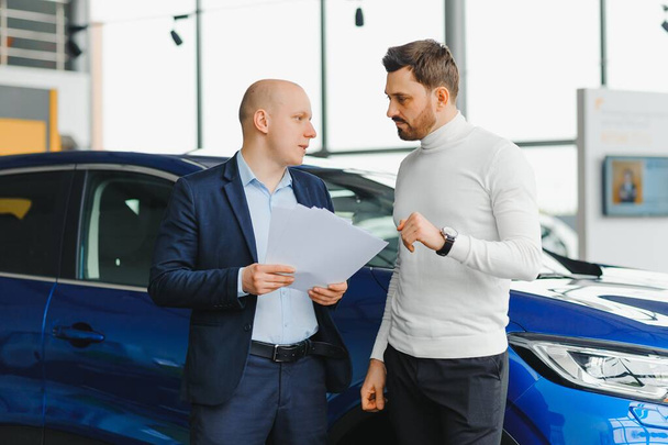 Salesperson selling cars at car dealership - Фото, изображение
