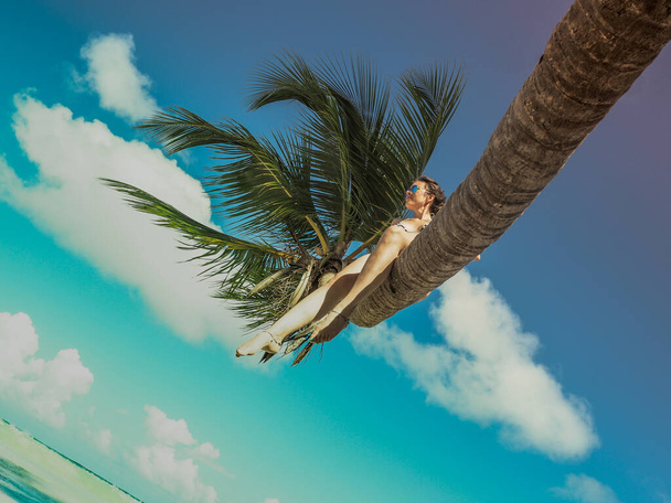 young carefree woman sitting on palm tree at tropical beach - Fotó, kép