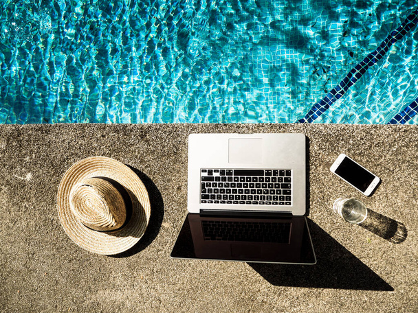 straw hat, laptop and mobile phone at poolside - Photo, Image