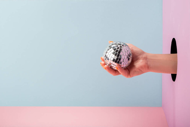 Womans hand holding a disco ball on blue and pink background - Zdjęcie, obraz