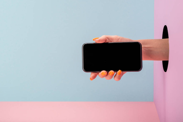 Womans hand holding a phone on blue and pink background - Photo, image