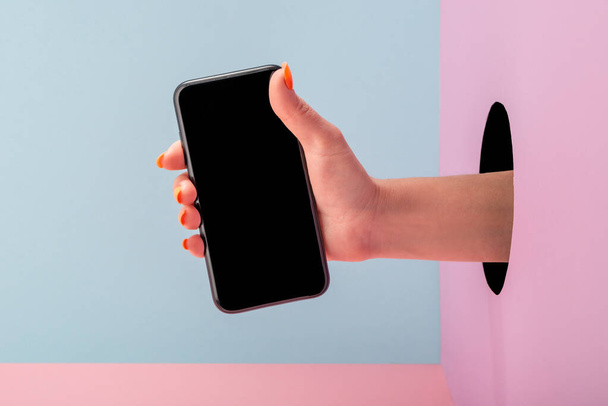 Close-up on womans hand holding a phone on blue and pink background - Zdjęcie, obraz