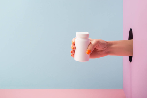 Womans hand holding a white bottle of pills on blue and pink background - Foto, Imagem