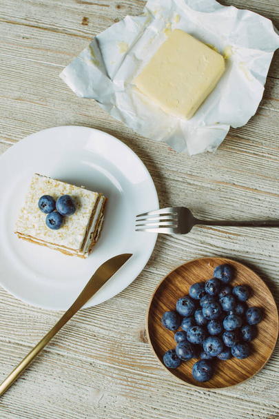 Medový dort s borůvkami a máslem na bílém podšálku na stole - Fotografie, Obrázek