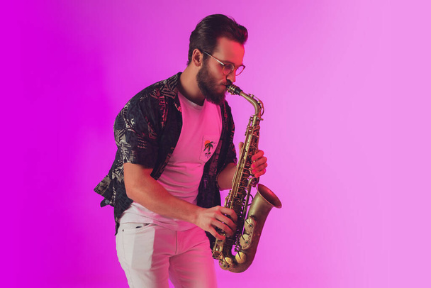 Young caucasian jazz musician playing the saxophone in neon light - Fotoğraf, Görsel