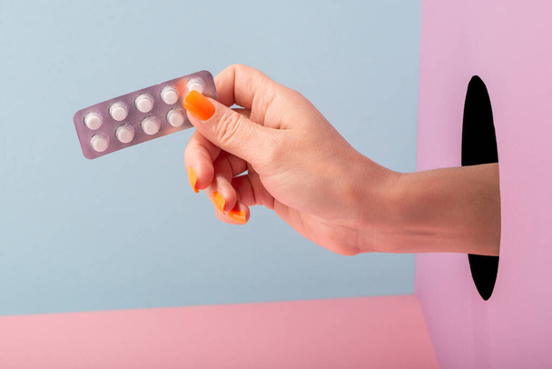 Close-up on womans hand holding a blister of pills on blue and pink background - Fotografie, Obrázek