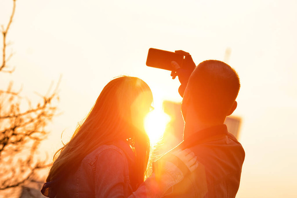 Young tourist couple using smart tablet in urban city environment for taking photos in sunset / sunrise time. - Valokuva, kuva