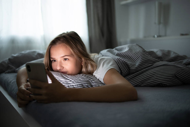 Pretty, young woman sleeping in her bed with her cell phone close to her. Smartphone in Bed Mobile/smartphone  Addiction Concept. - Foto, imagen
