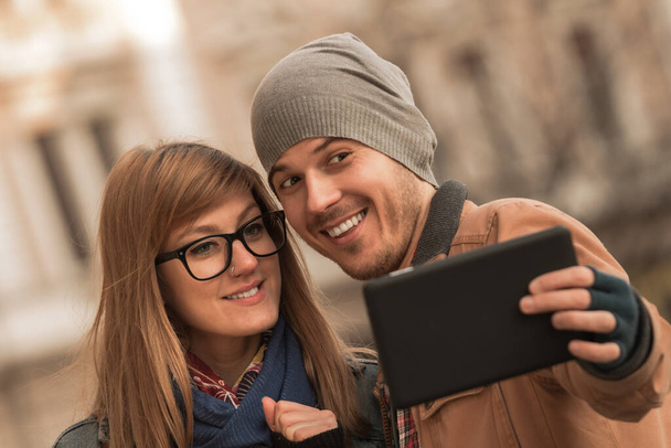 Młoda para turystów korzystająca z tabletu inteligentnego w środowisku miejskim do robienia zdjęć. - Zdjęcie, obraz