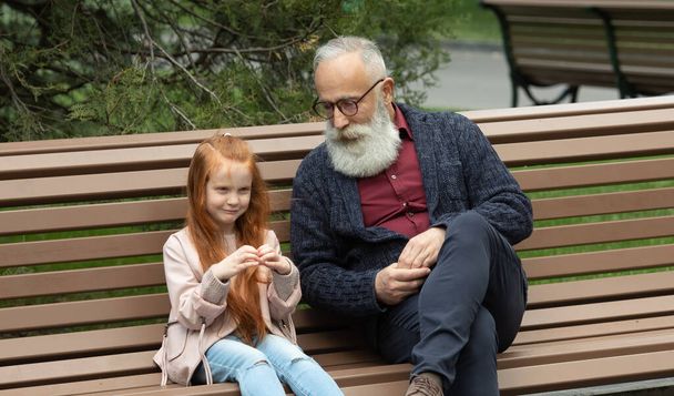Happy bearded grandfather and red hair granddaughter outdoor. - Foto, Imagen