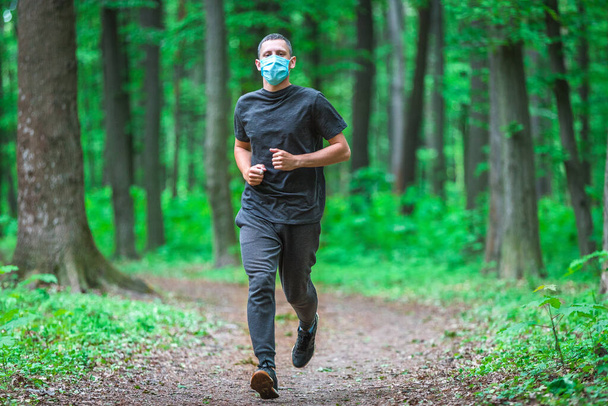 Runner wearing medical mask. Coronavirus pandemic Covid-19 a man in a medical mask runs in the forest - Φωτογραφία, εικόνα