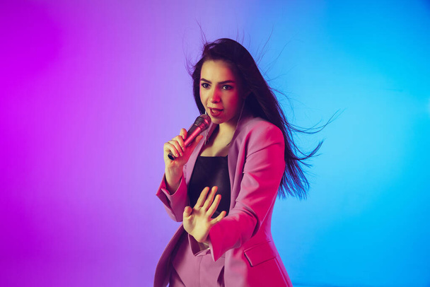 Caucasian female singer portrait isolated on gradient studio background in neon light - Foto, Bild
