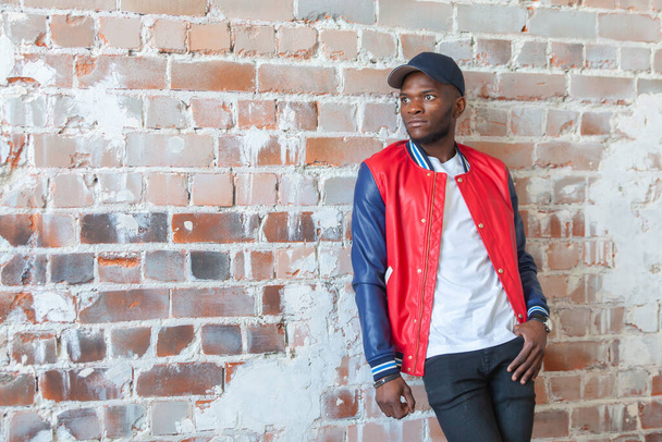 Bell'uomo africano in abiti casual e un berretto è in piedi in baraccopoli sullo sfondo del muro di mattoni rossi in rovina
 - Foto, immagini