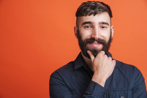 Image closeup of happy stylish man with nose jewelry wearing black shirt smiling at camera isolated over orange background - Foto, afbeelding