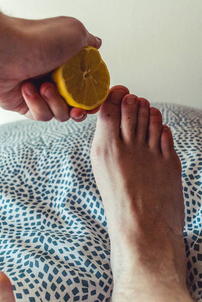 Mano sosteniendo un limón amarillo con unos pequeños pies jóvenes sobre una cama
. - Foto, imagen