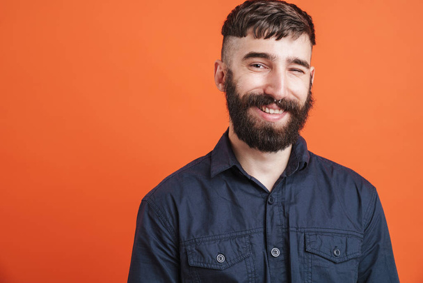 Image closeup of positive stylish man with nose jewelry wearing black shirt smiling at camera isolated over orange background - Foto, imagen