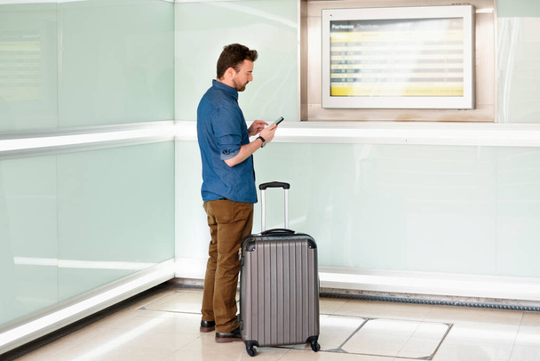 Man with carry on roller in modern corridor looking timetable - Foto, Imagen