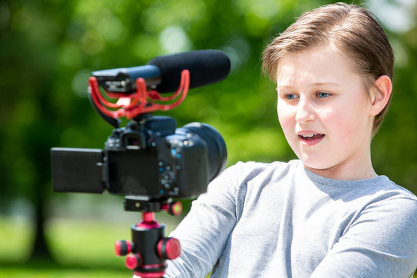 Blogging e vlogging conceito, menino sorridente feliz ou blogueiro com câmera de gravação de vídeo blog na floresta exterior
 - Foto, Imagem
