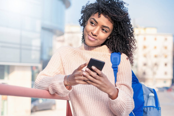 Feliz joven mujer negra sosteniendo el teléfono celular al aire libre en la ciudad
 - Foto, Imagen