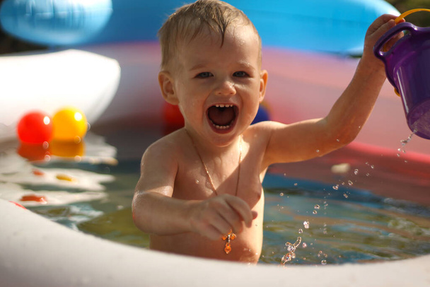 Naurava poika lasten altaassa. Aurinkoinen kesätunnelmakuva. Iloinen lapsi leikkii uima-altaassa pisaroilla vettä kirkkaan auringonpaisteen alla
. - Valokuva, kuva