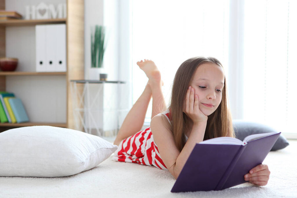 маленька дівчинка читає книжку вдома
 - Фото, зображення