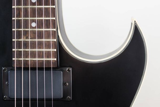 ブラック・エレキ・ロック・ギター、ハンバッカー・ピックアップ付きでマクロ・ショット。白い壁の背景に流線型の楽器の形状シルエット. - 写真・画像