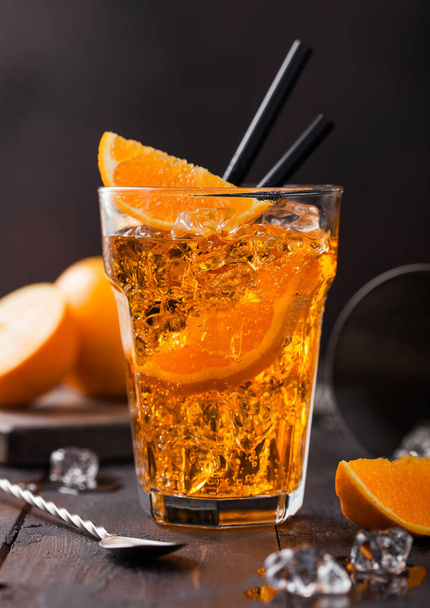 Aperol spritz summer cocktail in highball glass with orange slices and bar spoon on black background with ice cubes. Cocktail shaker with iace cubes and strainer - Φωτογραφία, εικόνα