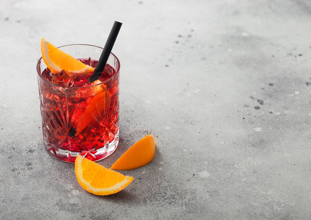 Negroni cocktail in crystal glass with orange slice and black straw on light table background. Top view - Фото, изображение