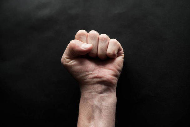La mano de un hombre apretó un puño sobre un fondo negro. Arte de protesta. Un símbolo de la lucha
 - Foto, imagen