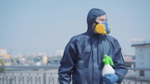 Middle shot of tired worker in biohazard suit walking along city street with disinfectant spray. Portrait of exhausted Caucasian man disinfecting public places on hot summer days. Covid-19 pandemic. - 映像、動画