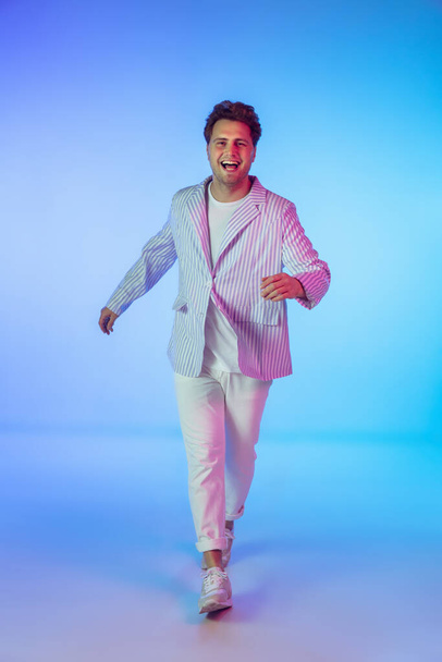 Young caucasian musician, dancer, party host, DJ on gradient background in neon light - Foto, afbeelding
