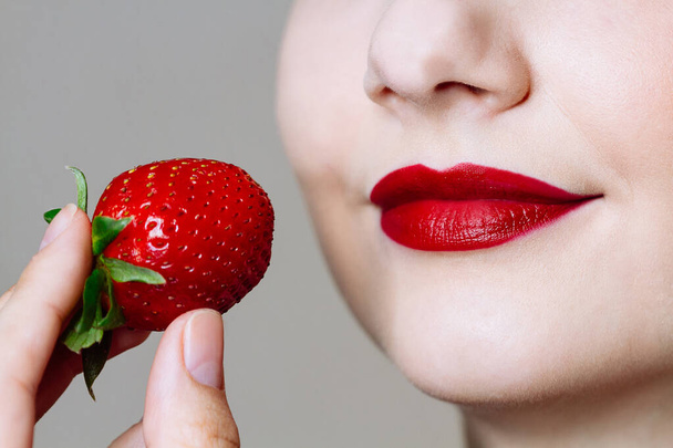 Macro close up of caucasus woman's lips with red lipstick and fresh strawberry. Food pleasure, healthy food concept - 写真・画像
