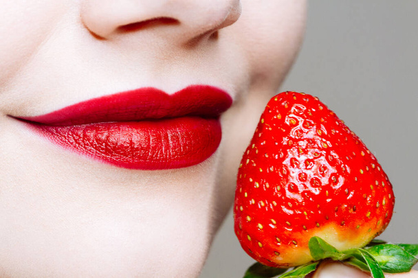 Macro close up of caucasus woman's lips with red lipstick and fresh strawberry. Food pleasure, healthy food concept - Foto, afbeelding