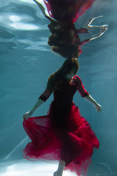 Beautiful girl underwater in a red dress swims in the pool. Tenderness and elegance. Bubbles and a lot of water - Foto, imagen
