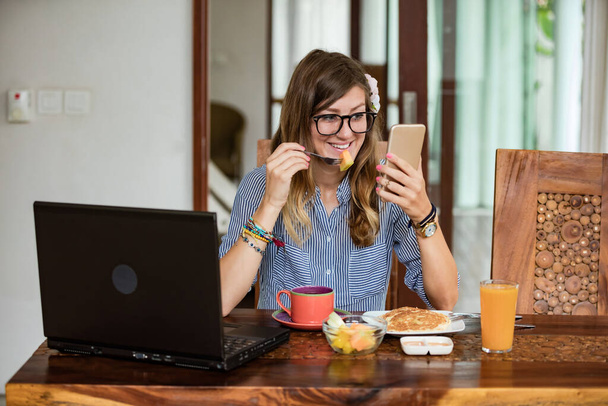 Vrouw die thuis laptop en mobiele telefoon gebruikt tijdens het ontbijt - freelancing concept. - Foto, afbeelding