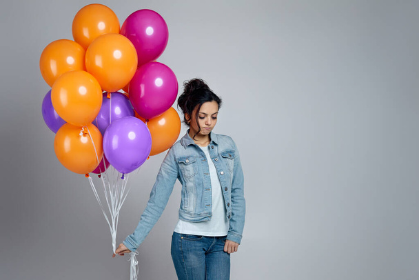 sad girl in denim posing with bright colorful air balloons - Foto, imagen