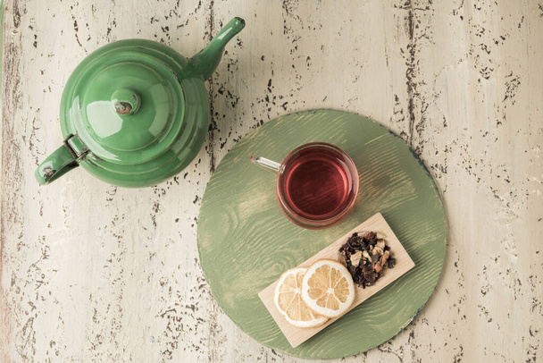a glass of herbal tea and vintage enamel teapot on a wooden table - Photo, Image