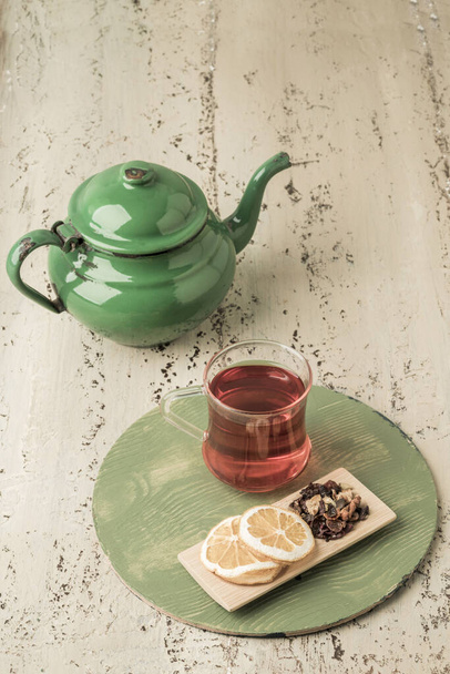 a glass of herbal tea and vintage enamel teapot on a wooden table - Photo, Image
