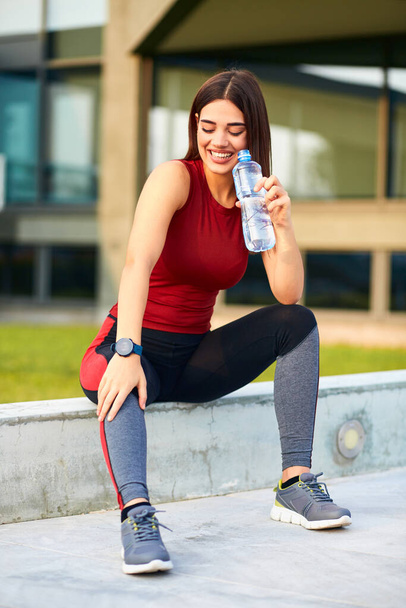 Thirsty young sporty woman making pause and drinking water during exerising. - Photo, image