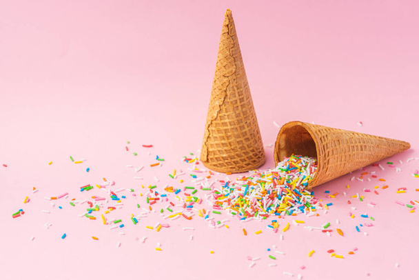 Два конуса мороженого из пшеничной муки один вверх ногами, а другой наполнен цветным сахаром на розовом фоне. Летняя концепция
. - Фото, изображение