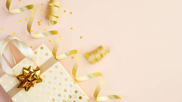 Happy birthday or party background. Flat lay composition with golden confetti, party streamers, bag with gift on beige table. Top view. - Foto, imagen