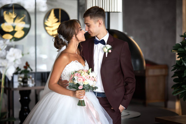Schöne Braut im weißen Kleid und ein hübscher Bräutigam im weinroten Anzug schauen einander an - Foto, Bild