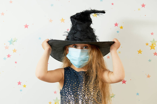 Happy Halloween on quarantine coronavirus pandemic. Little girl child in witch carnival costume and face protection mask. - Фото, зображення