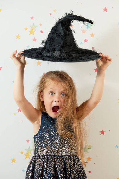 Happy Halloween. Little girl child in witch carnival costume and black hat. Funny face - Фото, изображение