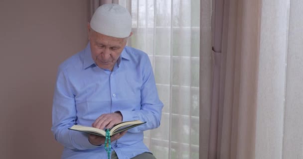 An old muslim man reading Koran at home - Materiał filmowy, wideo