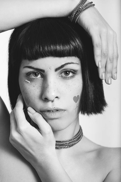 Çilli ve kalp şeklinde çıkartmalı genç bir kadının portresi. Eller geometrik pozisyonda. Siyah ve beyaz - Fotoğraf, Görsel