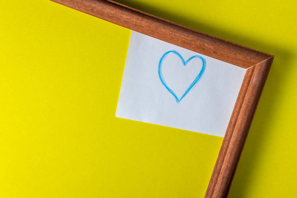 kehys keltaisella pohjalla. rungon alla on paperinpala ja maalattu sininen sydän
 - Valokuva, kuva