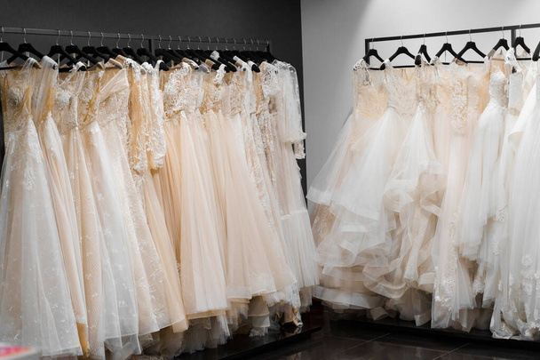 Menyasszonyi ruhák selyem sifonból, tüllből és csipkéből. Gyönyörű fehér krém menyasszonyi ruha vállfán esküvői szalonban. Gyöngyök és kristályok medálok az ingujján egy finom színű esküvői ruha - Fotó, kép