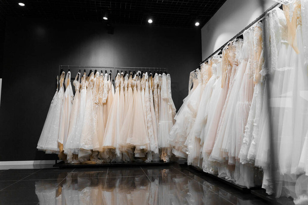 Menyasszonyi ruhák selyem sifonból, tüllből és csipkéből. Gyönyörű fehér krém menyasszonyi ruha vállfán esküvői szalonban. Gyöngyök és kristályok medálok az ingujján egy finom színű esküvői ruha - Fotó, kép